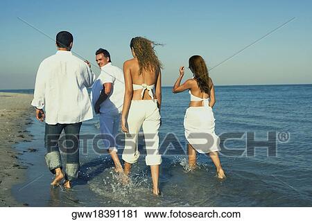 Rear view of two young women and a young man with a mid adult man walking on the beach View Large Photo Image Stock Image - Rear view of two young women and a young man with a mid adult man walking on the beach. Fotosearch