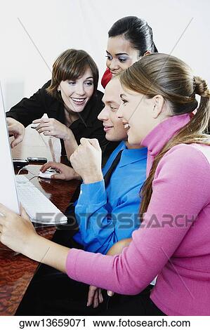 Stock Image - Side profile of a businessman and three businesswomen using a desktop PC. Fotosearch