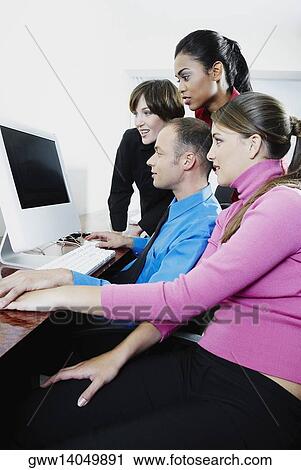 Stock Image - Side profile of a businessman and three businesswomen using a desktop PC. Fotosearch
