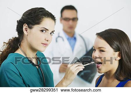 Stock Image - Side profile of a female doctor examining a girl's mouth with a tongue depressor. Fotosearch