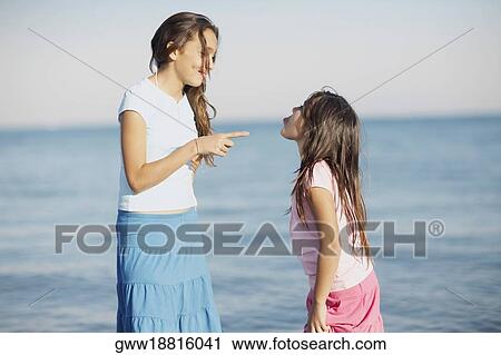 Stock Image - Side profile of a girl pointing to her sister. Fotosearch