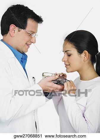 Stock Image - Side profile of a male doctor giving eyeglasses to a female patient. Fotosearch