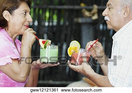 Side profile of a mature couple sitting and holding glasses of juice View Large Photo Image Stock Image - Side profile of a mature couple sitting and holding glasses of juice. Fotosearch