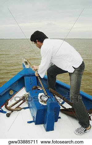 Stock Image - Side profile of a mid adult man pulling a chain in a boat. Fotosearch