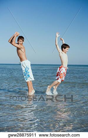 Side profile of a teenage boy playing with his brother in water with their arms raised View Large Photo Image Stock Image - Side profile of a teenage boy playing with his brother in water with their arms raised. Fotosearch