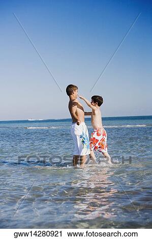 Side profile of a teenage boy standing with his brother in water View Large Photo Image Stock Image - Side profile of a teenage boy standing with his brother in water. Fotosearch