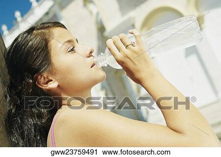 Stock Image - Side profile of a teenage girl drinking water from a bottle. Fotosearch