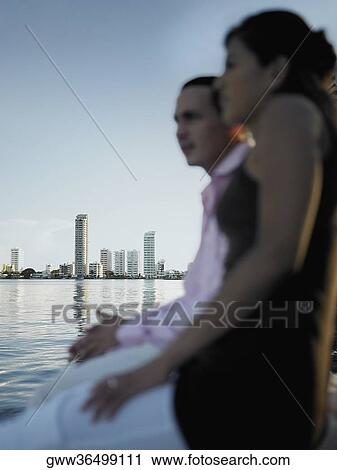 Side profile of a young couple sitting on a pier View Large Photo Image Stock Image - Side profile of a young couple sitting on a pier. Fotosearch
