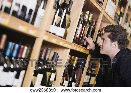 Side profile of a young man choosing wine bottle from a rack in a liquor store View Large Photo Image Stock Image - Side profile of a young man choosing wine bottle from a rack in a liquor store. Fotosearch