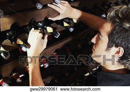 Side profile of a young man taking a bottle from a wine rack View Large Photo Image Stock Image - Side profile of a young man taking a bottle from a wine rack. Fotosearch