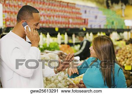 Stock Image - Side profile of a young man talking on a mobile phone and a young woman looking at him. Fotosearch