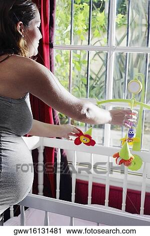 Side profile of a young pregnant woman adjusting toys over a crib View Large Photo Image Stock Image - Side profile of a young pregnant woman adjusting toys over a crib. Fotosearch