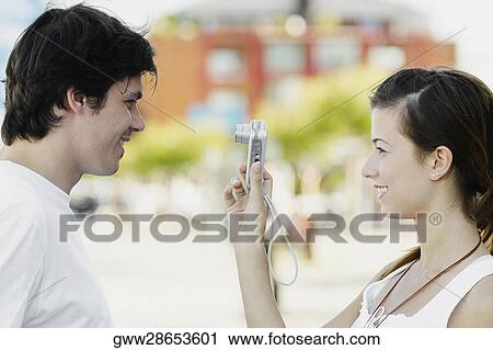 Side profile of a young woman taking a snapshot of a young man View Large Photo Image Stock Image - Side profile of a young woman taking a snapshot of a young man. Fotosearch