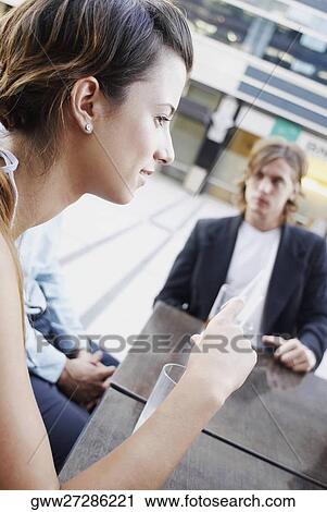 Stock Image - Side profile of a young woman with her friends sitting in a restaurant. Fotosearch