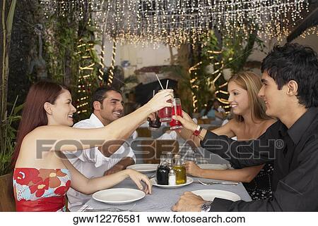 Stock Image - Side profile of four people sitting at a table and toasting with glasses. Fotosearch