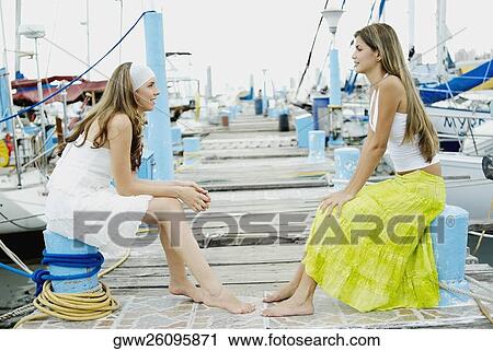 Side profile of two young women sitting at a dock and looking at each other View Large Photo Image Stock Image - Side profile of two young women sitting at a dock and looking at each other. Fotosearch