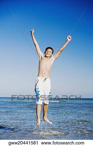 Stock Image - Teenage boy jumping in water with his arms raised. Fotosearch