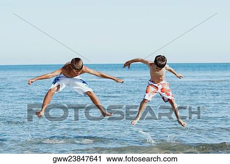 Teenage boy jumping with his brother in water with their arms outstretched View Large Photo Image Stock Image - Teenage boy jumping with his brother in water with their arms outstretched. Fotosearch