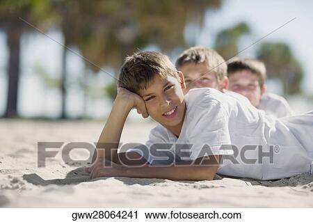 Two boys and a teenage boy lying on the beach View Large Photo Image Stock Image - Two boys and a teenage boy lying on the beach. Fotosearch