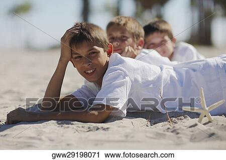 Two boys and a teenage boy lying on the beach View Large Photo Image Stock Image - Two boys and a teenage boy lying on the beach. Fotosearch