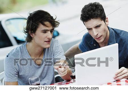 Two young men sitting at a table and using a laptop View Large Photo Image Stock Image - Two young men sitting at a table and using a laptop. Fotosearch