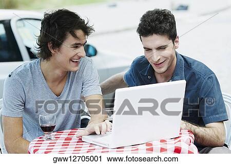 Stock Image - Two young men using a laptop and smiling. Fotosearch