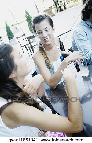 Stock Image - Two young women and a man sitting together in a sidewalk cafe. Fotosearch