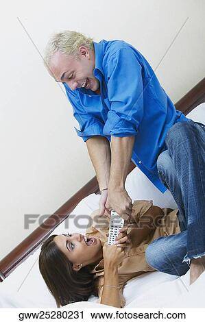 Young couple fighting for a remote control on the bed View Large Photo Image Stock Image - Young couple fighting for a remote control on the bed. Fotosearch
