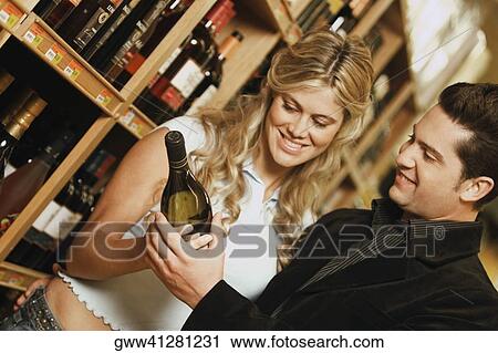Stock Image - Young couple holding a wine bottle in a liquor store. Fotosearch