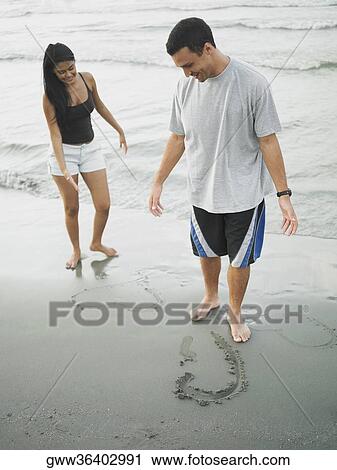 Young couple standing on the beach and looking down View Large Photo Image Stock Image - Young couple standing on the beach and looking down. Fotosearch
