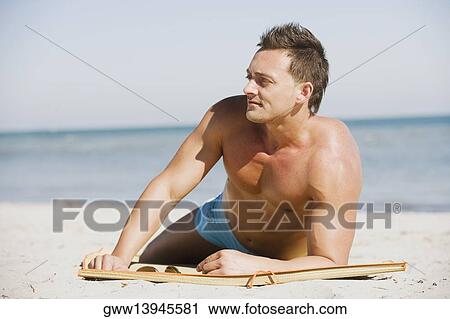 Young man lying on the beach and looking away View Large Photo Image Stock Image - Young man lying on the beach and looking away. Fotosearch