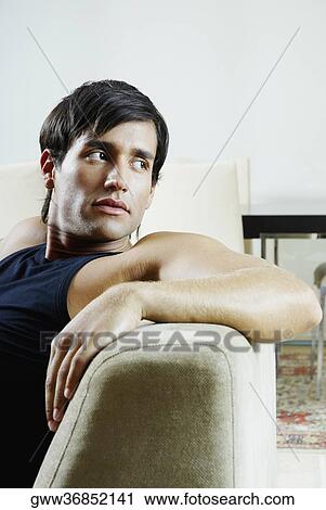 Young man sitting on a couch and looking sideways View Large Photo Image Stock Image - Young man sitting on a couch and looking sideways. Fotosearch