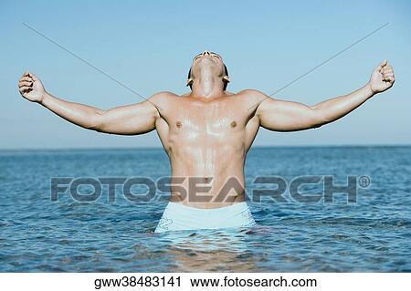 Young man standing in water with his arms outstretched View Large Photo Image Stock Image - Young man standing in water with his arms outstretched. Fotosearch