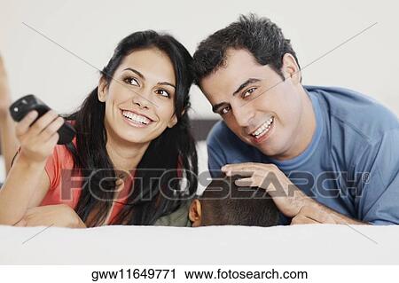 Young woman and a mid adult man lying down with their son on the bed and smiling View Large Photo Image Stock Image - Young woman and a mid adult man lying down with their son on the bed and smiling. Fotosearch