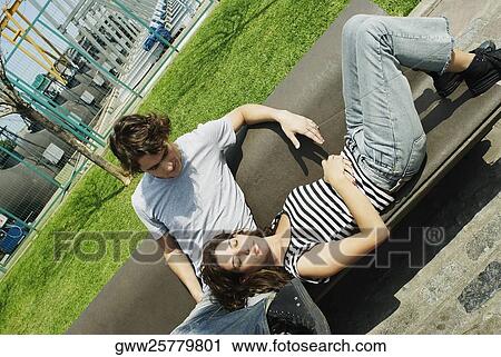 Young woman lying on a bench resting her head in the lap of a young man View Large Photo Image Stock Image - Young woman lying on a bench resting her head in the lap of a young man. Fotosearch