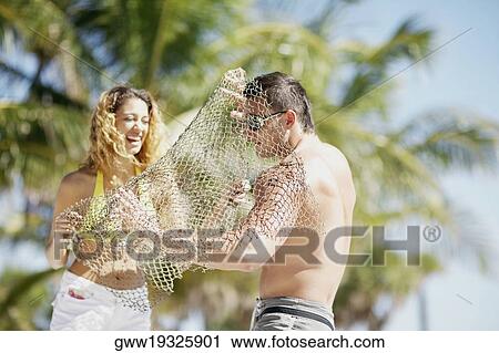 Stock Image - Young woman putting a fishing net over a young man and smiling. Fotosearch