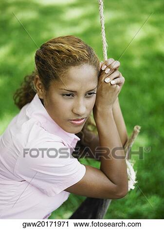 Stock Image - Young woman sitting on a rope swing. Fotosearch