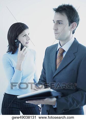 Stock Image - Businessman holding a personal organizer with a businesswoman talking on a mobile phone behind him. Fotosearch