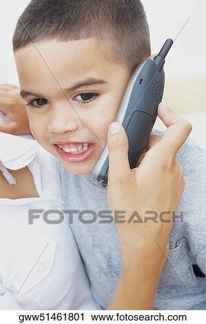 Stock Image - Close-up of a boy sitting on his mother's lap and talking on a mobile phone. Fotosearch