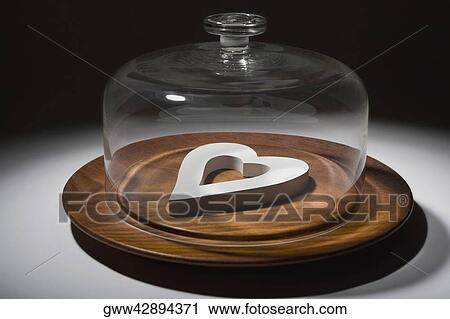 Stock Image - Close-up of a glass container covering a heart shaped object on a dish. Fotosearch