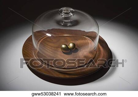 Stock Image - Close-up of a glass container covering a pair of golden eggs on a dish. Fotosearch
