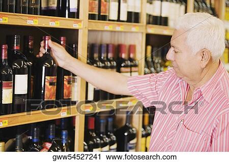 Stock Image - Close-up of a mature man holding a wine bottle in a liquor store. Fotosearch