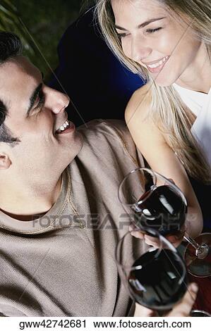 Stock Image - Close-up of a mid adult man and a mid adult woman holding glasses of red wine and smiling. Fotosearch