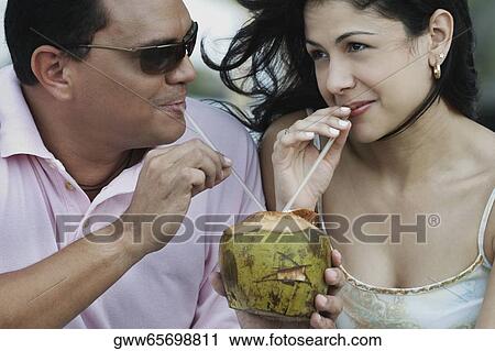 Close-up of a mid adult man and a young woman drinking coconut water View Large Photo Image Stock Image - Close-up of a mid adult man and a young woman drinking coconut water. Fotosearch