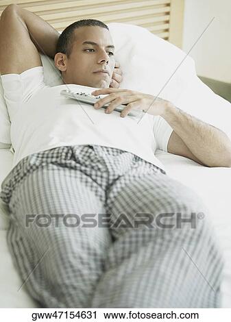 Close-up of a mid adult man lying on the bed and holding a remote control View Large Photo Image Stock Image - Close-up of a mid adult man lying on the bed and holding a remote control. Fotosearch