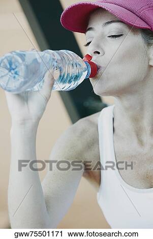 Stock Image - Close-up of a mid adult woman drinking water from a bottle. Fotosearch