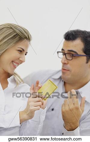 Close-up of a mid adult woman holding a credit card with a mid adult man looking at her View Large Photo Image Stock Image - Close-up of a mid adult woman holding a credit card with a mid adult man looking at her. Fotosearch