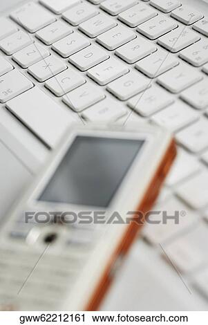 Stock Image - Close-up of a mobile phone on a laptop. Fotosearch