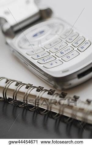 Stock Image - Close-up of a mobile phone on a spiral notebook. Fotosearch