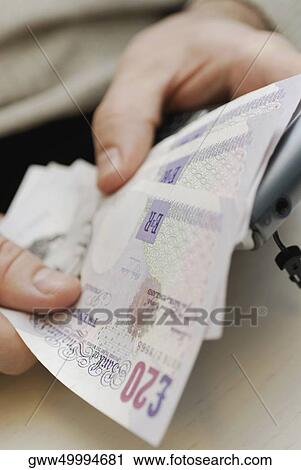 Stock Image - Close-up of a person counting twenty pound notes. Fotosearch